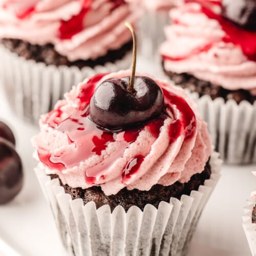 Black forest cupcakes on a serving plate topped with fresh cherries.