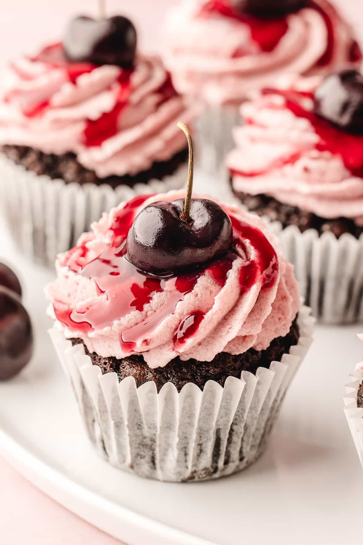 Black forest cupcakes on a serving plate topped with fresh cherries.