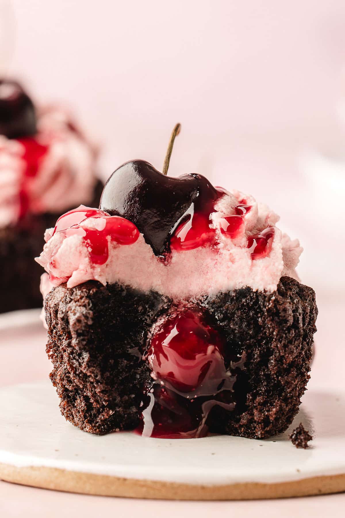 Two black forest cupcakes, one cut open with cherry filling coming from the middle.