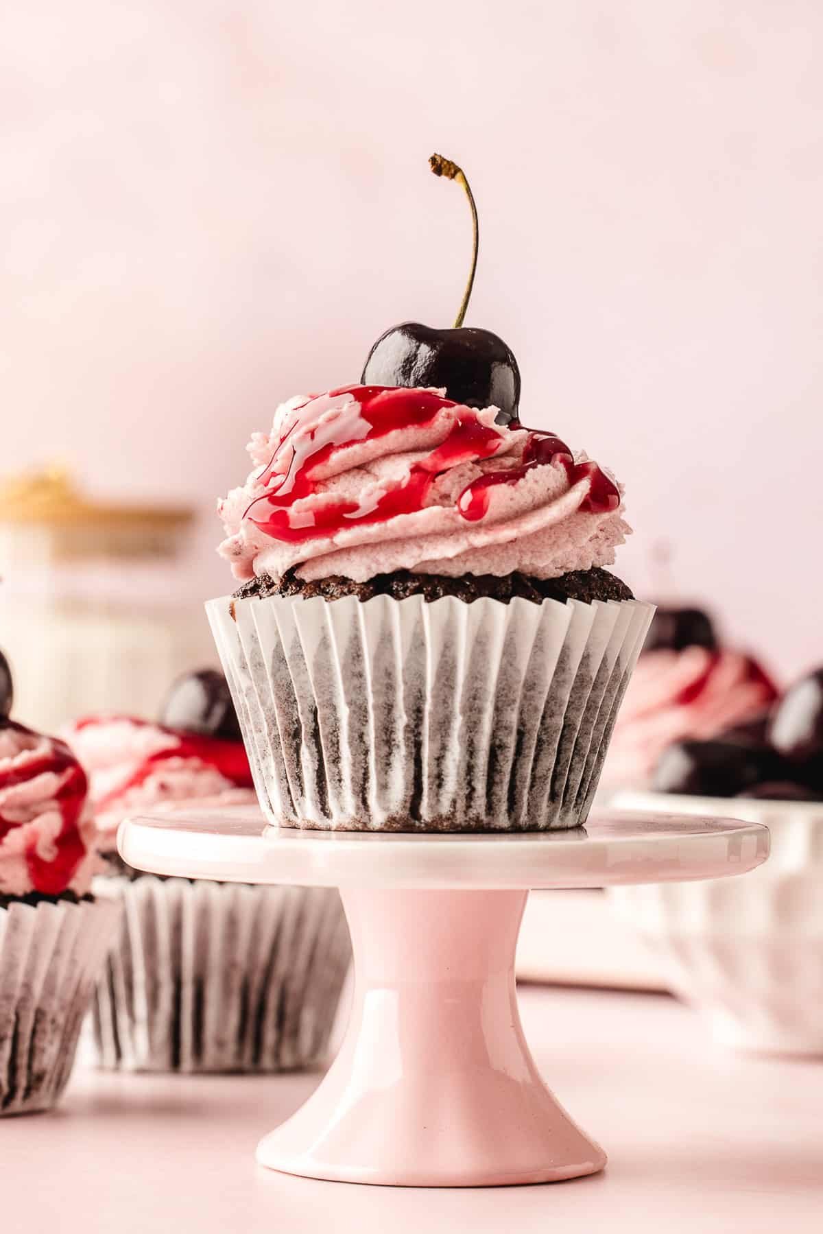 A chocolate cherry cupcake on a pedestal.
