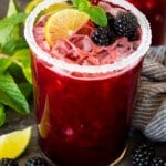 A glass of blackberry margarita topped with fresh berries, lime and mint.