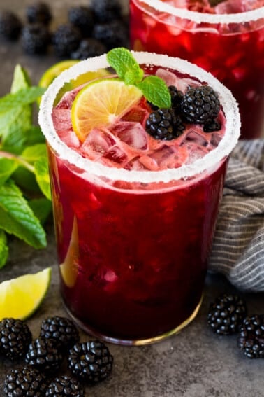 A glass of blackberry margarita topped with fresh berries, lime and mint.
