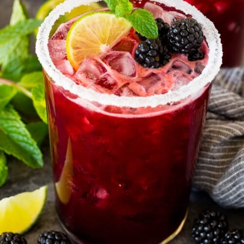 A glass of blackberry margarita topped with fresh berries, lime and mint.
