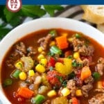 A bowl of hamburger soup garnished with parsley and served with bread.