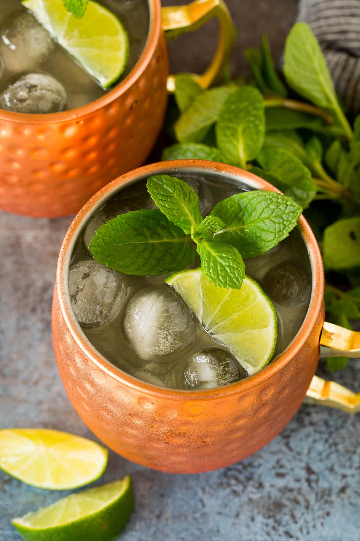 Two Mexican mule drinks garnished with lime wedges and mint sprigs.
