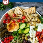A mezze platter featuring hummus, tzatziki sauce, olives, pita bread and veggies.
