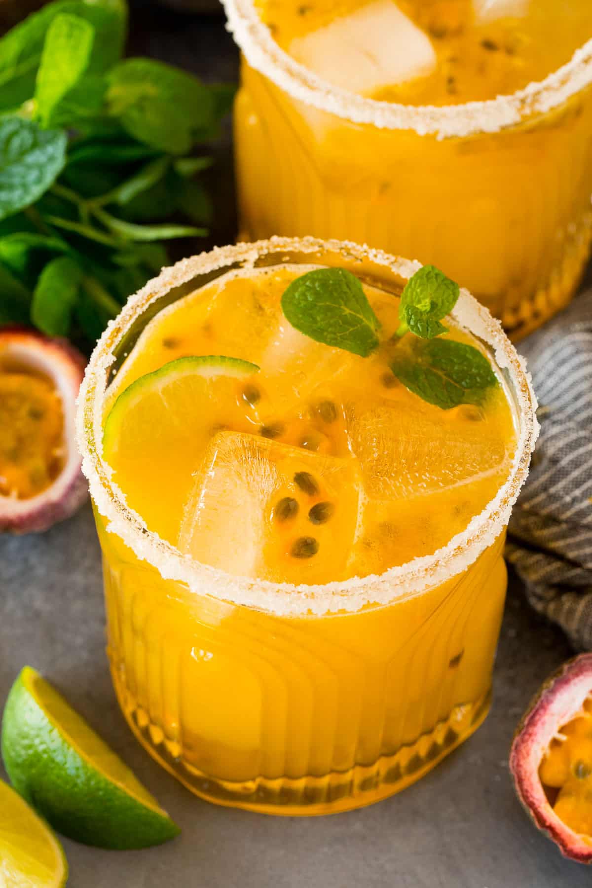 Two glasses of passion fruit margarita with sugared rims and mint for garnish.