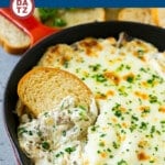 A skillet of Philly cheesesteak dip served with slices of toasted baguette bread.