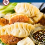 A plate of potstickers next to a small bowl of savory dipping sauce.