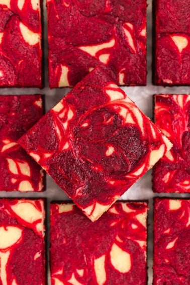 Red velvet brownies with a cheesecake swirl on a sheet of parchment paper.