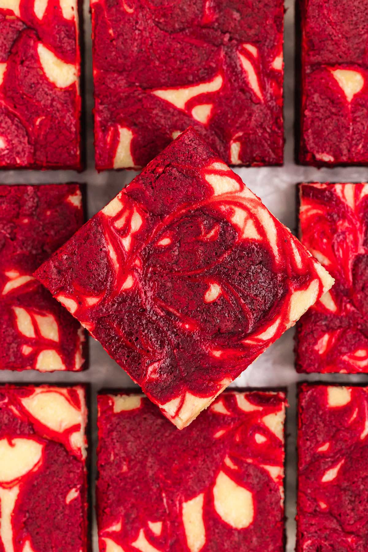 Red velvet brownies with a cheesecake swirl on a sheet of parchment paper.