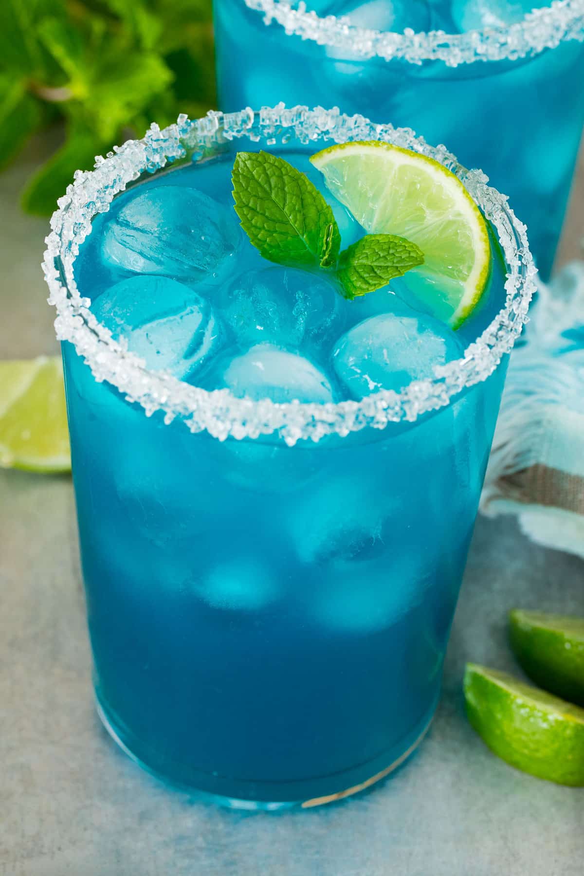A glass of blue margarita with a garnish of mint and lime slices.