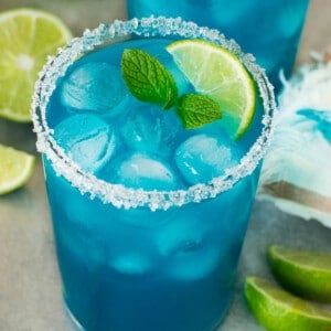 Two cups of blue margarita with a sugared rim and lime wedge for garnish.