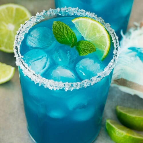 Two cups of blue margarita with a sugared rim and lime wedge for garnish.
