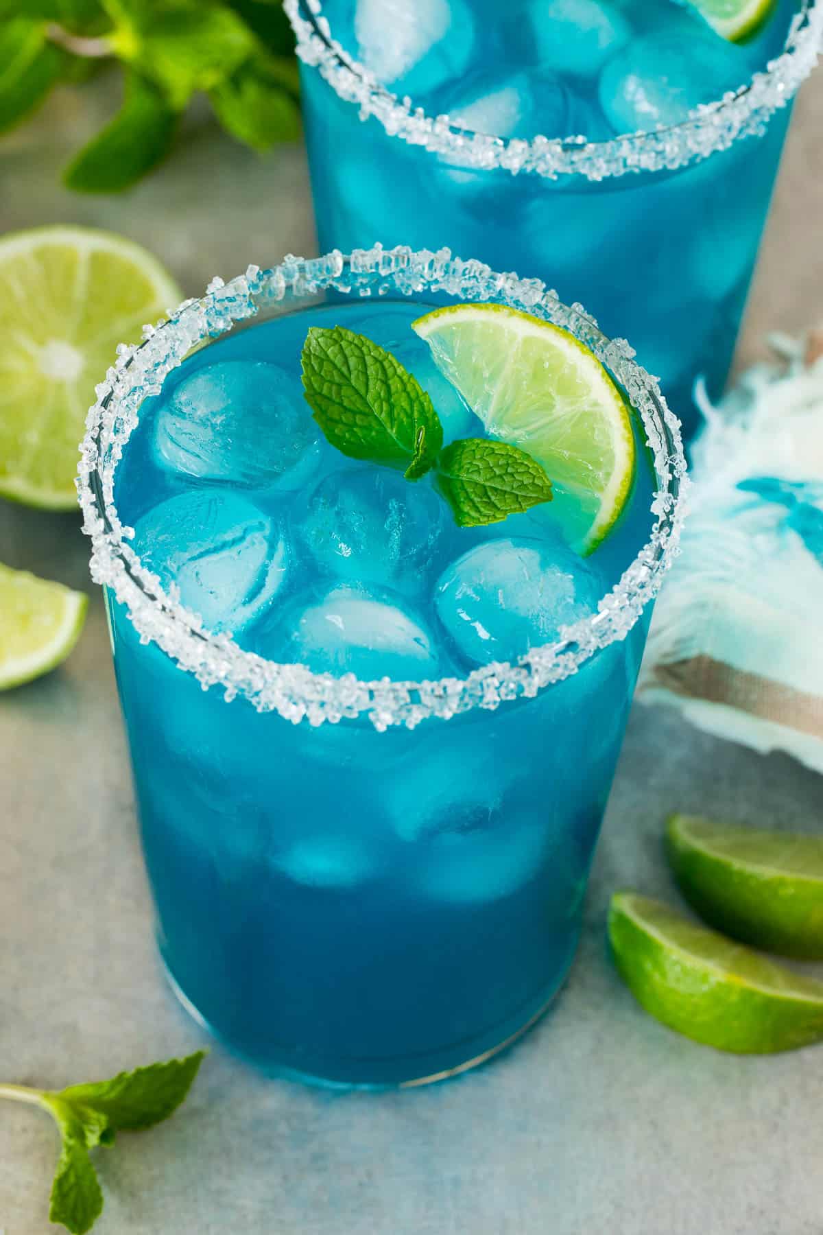 Two cups of blue margarita with a sugared rim and lime wedge for garnish.