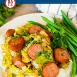 A plate of sausage and cabbage cooked on a skillet with mashed potatoes and green beans.