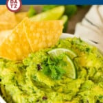 A bowl of Chipotle guacamole with lime slices on top and served with tortilla chips.