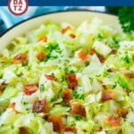 A skillet of fried cabbage with bacon garnished with parsley.