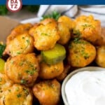 Several fried pickles on a plate garnished with parsley and dip.