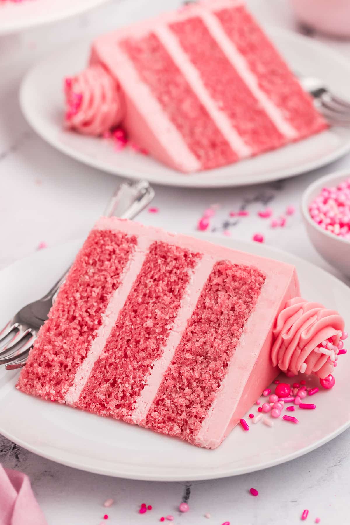 Slices of pink cake on plates with sprinkles on top.