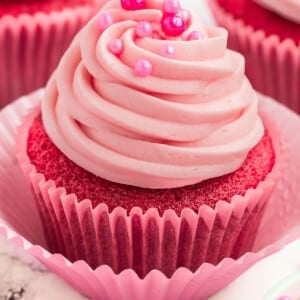 Pink cupcakes topped with pink cream cheese frosting and pearl sprinkles.