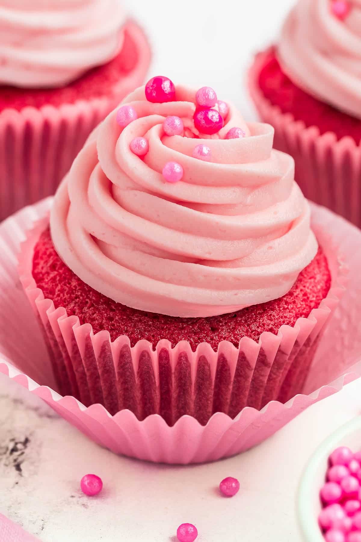 Pink cupcakes topped with pink cream cheese frosting and pearl sprinkles.