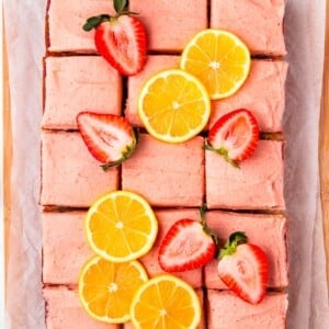 A strawberry lemon cake cut into squares and garnished with fresh berries and lemon slices.