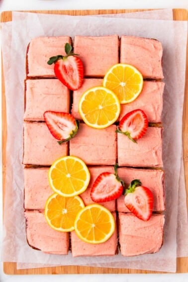 A strawberry lemon cake cut into squares and garnished with fresh berries and lemon slices.
