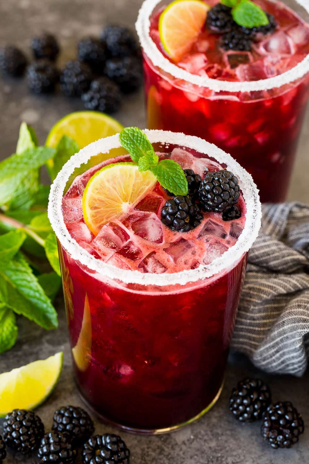 Two glasses of blackberry margarita with lime slices and mint sprigs as garnish.