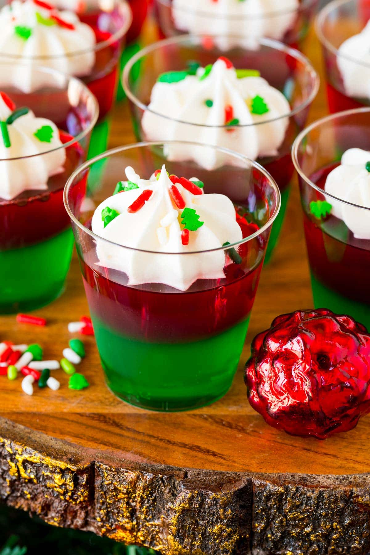 Christmas Jello shots topped with whipped cream and holiday sprinkles.