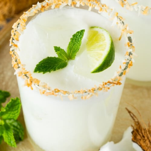 A glass of coconut margarita with a toasted coconut rim and a garnish of mint.