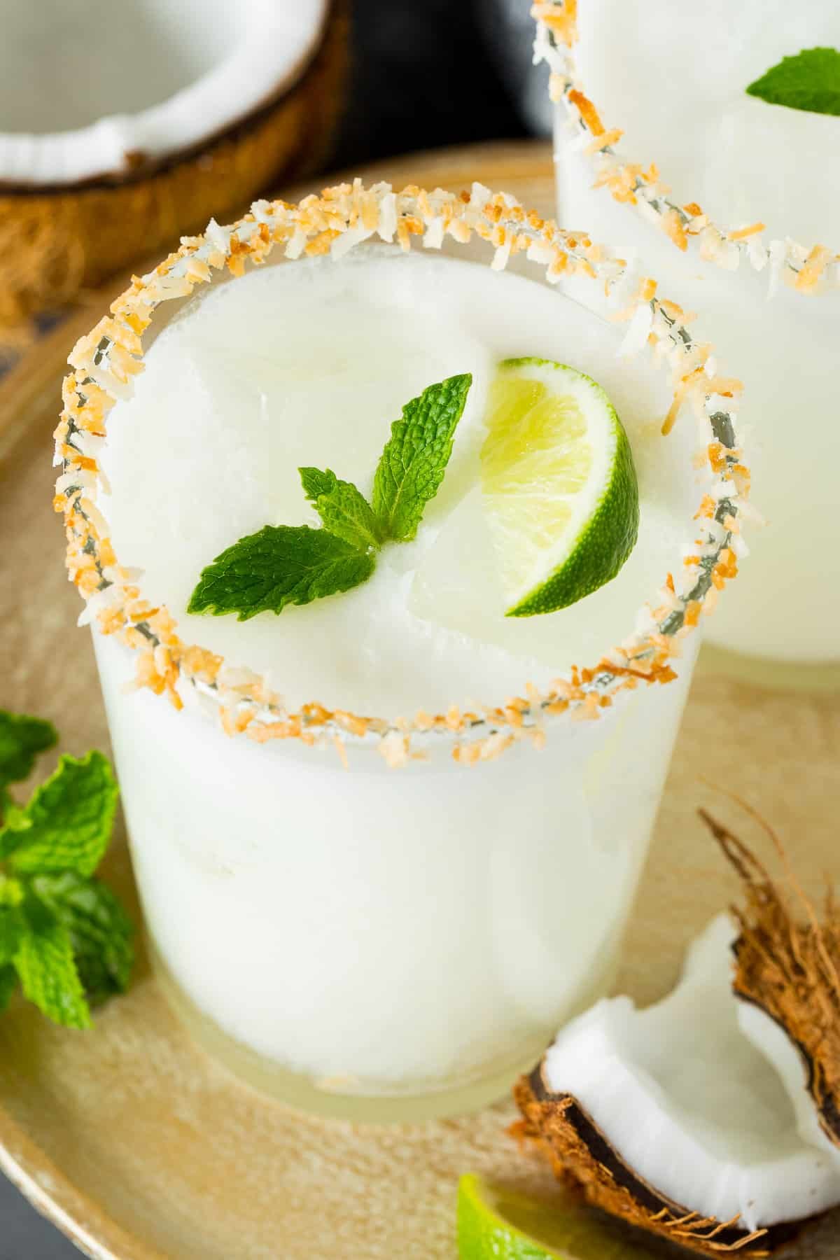 A glass of coconut margarita with a toasted coconut rim and a garnish of mint.