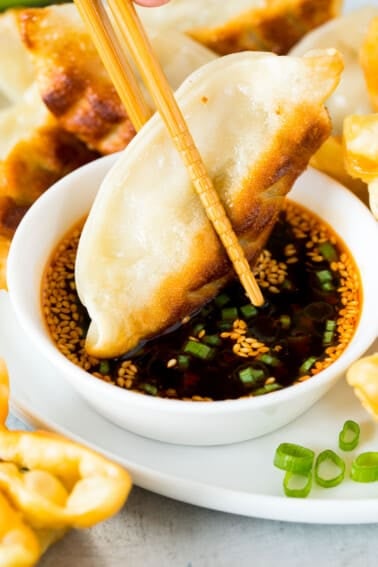 A potsticker being dipped into dumpling sauce with chopsticks.