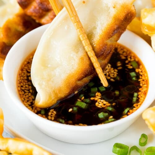A potsticker being dipped into dumpling sauce with chopsticks.