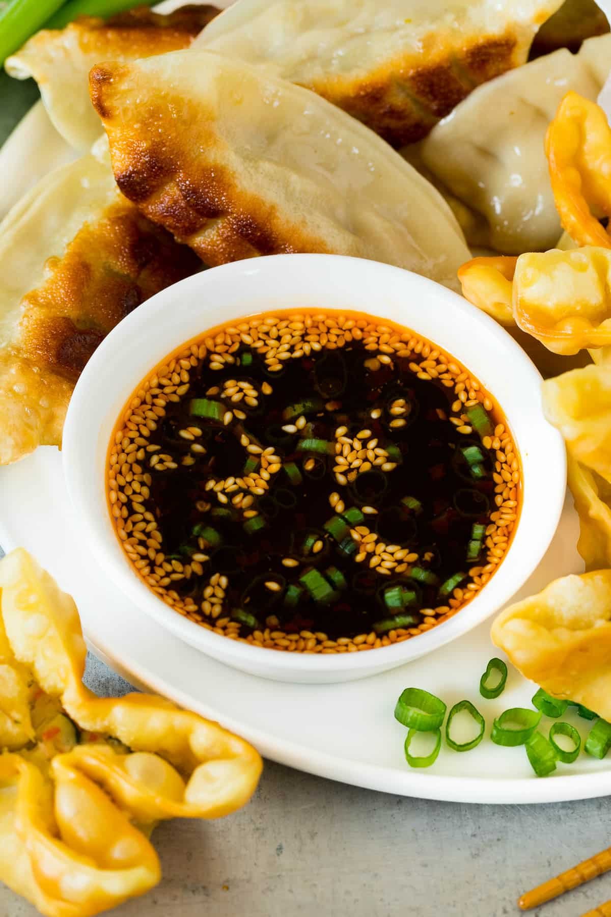 A bowl of dumpling sauce surrounded by wontons and dumplings.