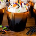 Orange and black layered Halloween Jello shots topped with whipped cream and sprinkles.