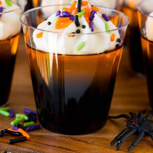 Orange and black layered Halloween Jello shots topped with whipped cream and sprinkles.