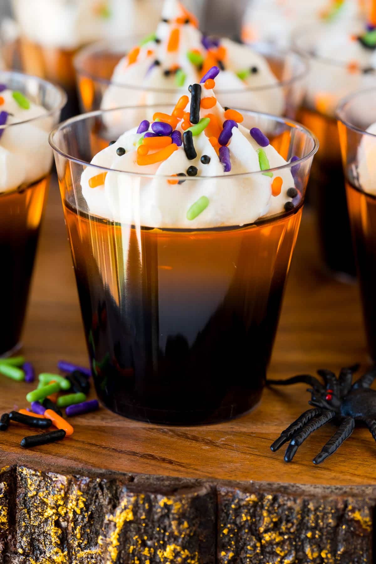 Orange and black layered Halloween Jello shots topped with whipped cream and sprinkles.