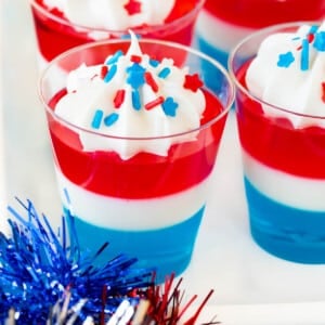 Red white and blue Jello shots topped with whipped cream and sprinkles.