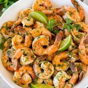 A serving bowl of cilantro lime shrimp with lime wedges in it.