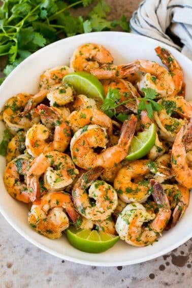 A serving bowl of cilantro lime shrimp with lime wedges in it.