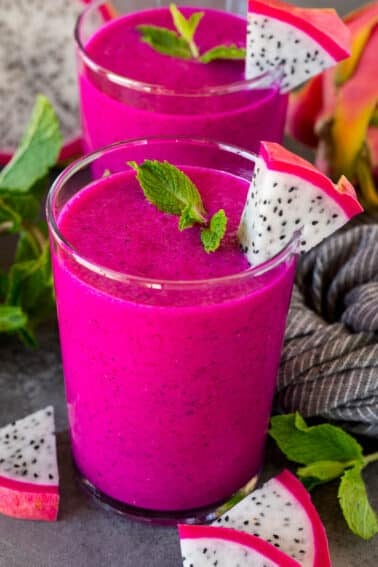 Two cups of dragon fruit smoothie topped with mint and fresh dragon fruit.