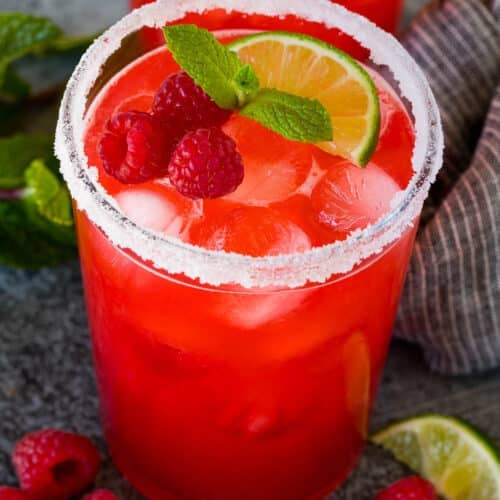 Glasses of raspberry margarita garnished with berries, mint and lime.