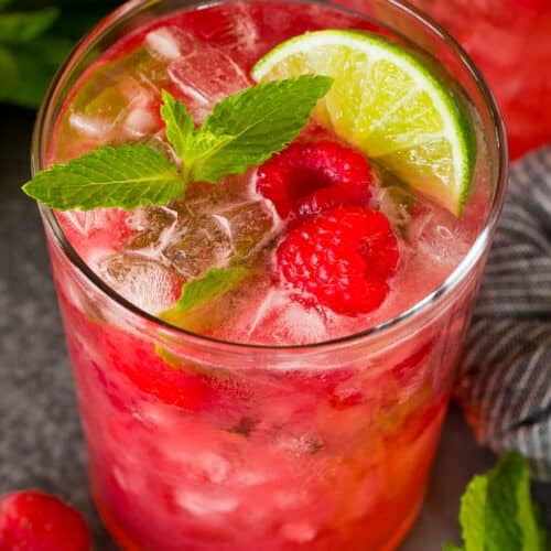 A raspberry mojito topped with fresh berries and a mint sprig.