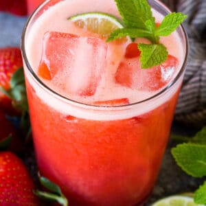 A glass of strawberry agua fresca garnished with mint and lime.