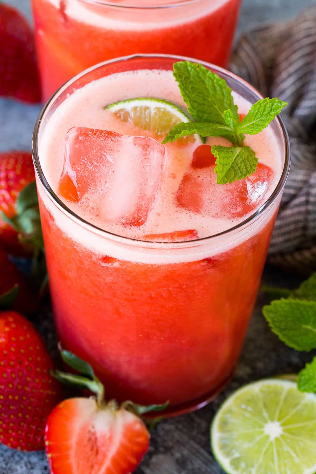 A glass of strawberry agua fresca garnished with mint and lime.