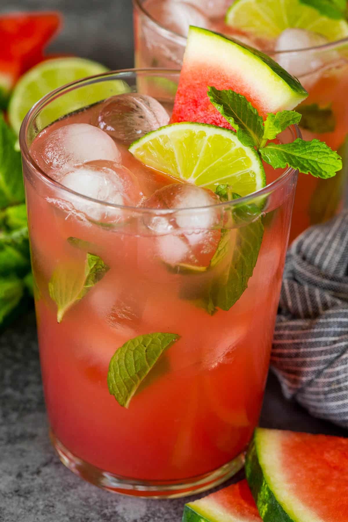 A glass of watermelon mojito with a slice of watermelon and lime wedge on top.