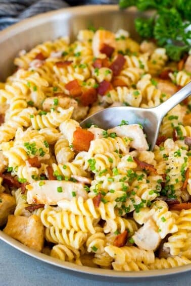 A skillet of chicken bacon ranch pasta with a serving spoon in it.