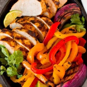 A platter of grilled chicken fajitas with onions, bell peppers, lime wedges and fresh cilantro.