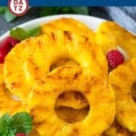 Grilled pineapple slices on a plate garnished with raspberries and mint leaves.